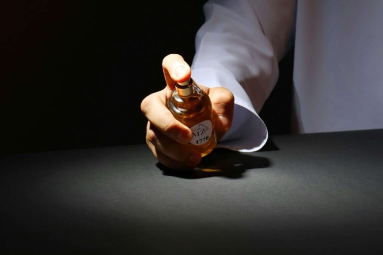 A hand elegantly holding a perfume bottle against a dark backdrop, highlighting luxury fragrance. Colognes
