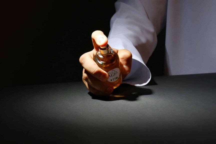 A hand elegantly holding a perfume bottle against a dark backdrop, highlighting luxury fragrance. Colognes