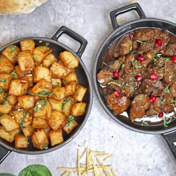 Tasty roast potatoes and beef stew garnished with herbs and pomegranate, perfect for a hearty meal. cast iron, carbon steel