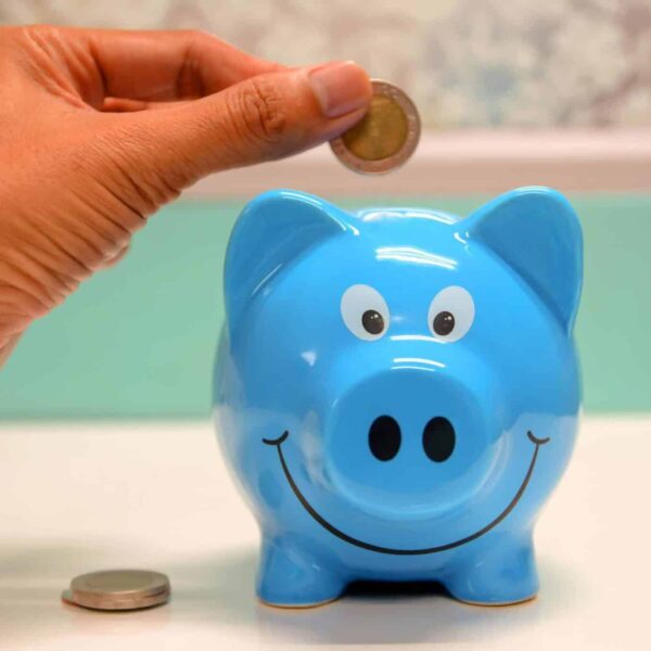 Hand inserting a coin into a blue piggy bank for savings and money management. Start with $50