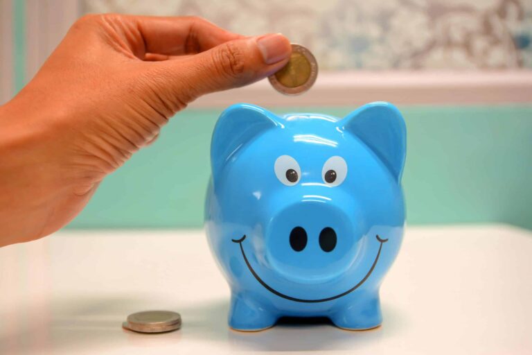 Hand inserting a coin into a blue piggy bank for savings and money management. Start with $50