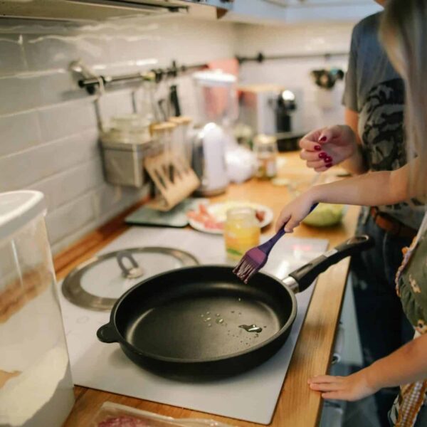 Young girl cooking with a frying pan under adult supervision in a modern kitchen. kitchen gadgets