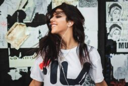 Portrait of a young woman smiling while listening to music with earphones against a graffiti wall. Most Anticipated Music Albums