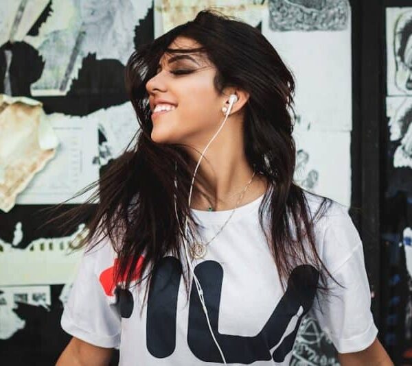 Portrait of a young woman smiling while listening to music with earphones against a graffiti wall. Most Anticipated Music Albums