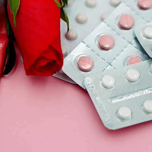 Pills and red rose on pink background, symbolizing healthcare and romance. hormonal birth control
