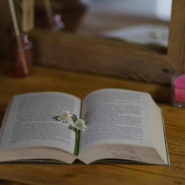 An open book with delicate flowers on a wooden table with a candle nearby. home sanctuary
