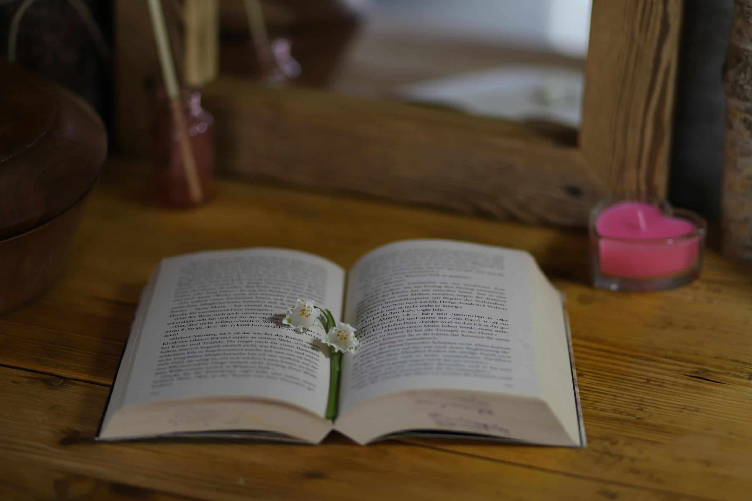 An open book with delicate flowers on a wooden table with a candle nearby. home sanctuary