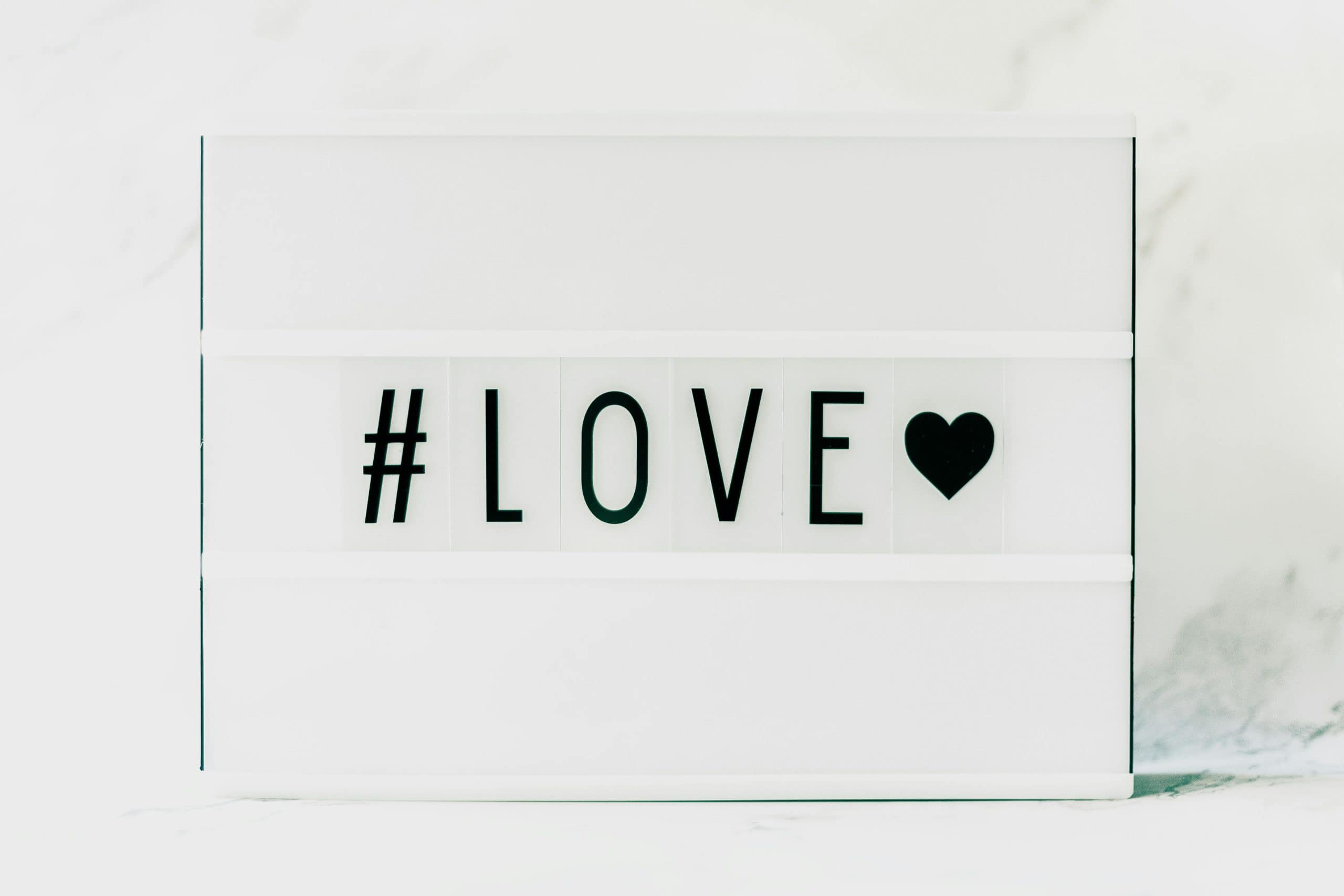 Contemporary minimalist sign displaying '#LOVE' in text with a black heart on a white background. venus in leo, love, bold love, emotional shifts,