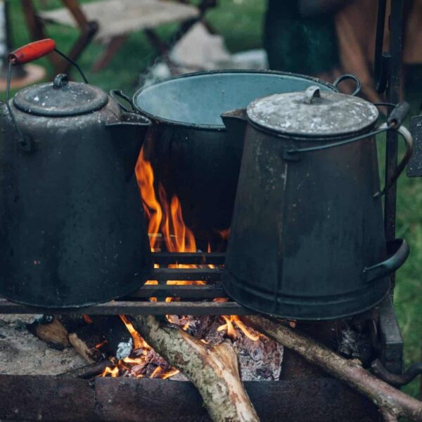Camp kettles and pot over open fire at an outdoor campsite, ideal for rustic cooking themes. Portable cooking gear for camping