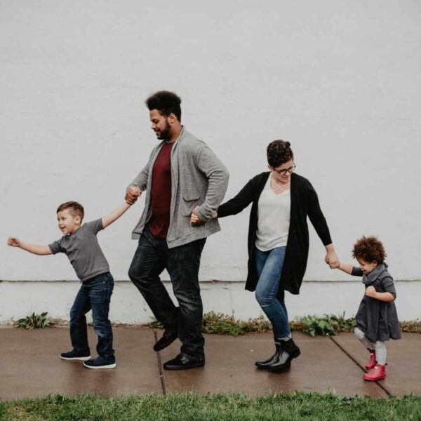 A joyful family walking together outdoors, holding hands in a playful and happy moment. Final days of summer.