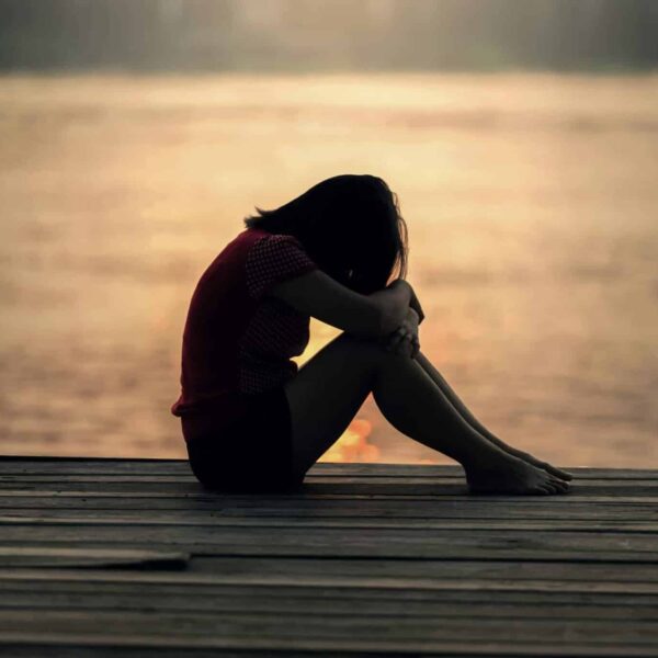 A woman sitting alone on a wooden dock by the lake, showing solitude and reflection.
