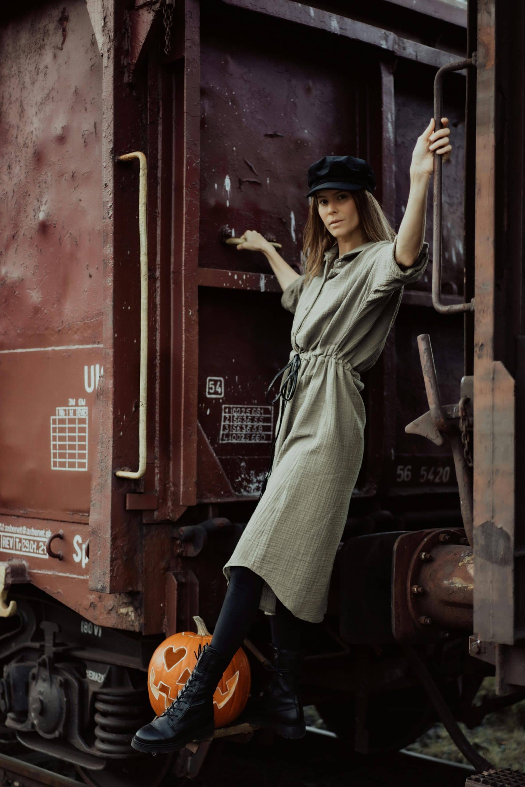 Woman posing in vintage attire on a train, with a Halloween pumpkin nearby.
