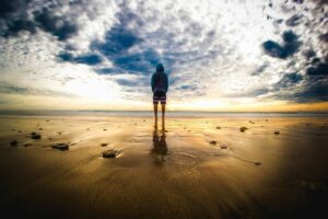 Cause to Pause: A lone figure stands on a tranquil beach during a vivid sunset, reflecting on the wet sand.