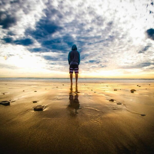 Cause to Pause: A lone figure stands on a tranquil beach during a vivid sunset, reflecting on the wet sand.