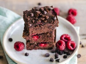 Close-up of deliciously indulgent chocolate raspberry brownies stacked on a ceramic plate with fresh raspberries. vegan desserts, refined sugar