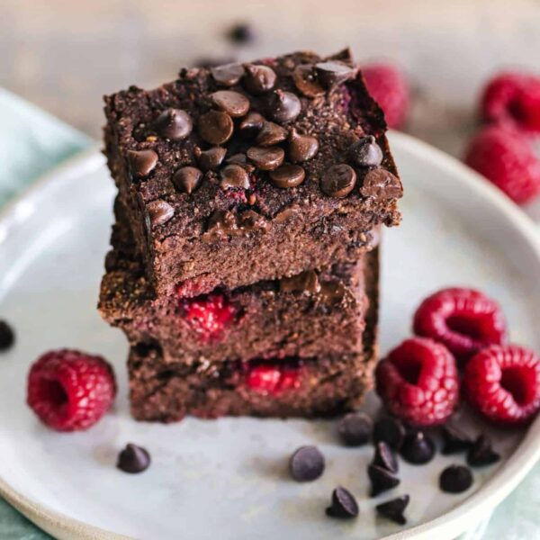 Close-up of deliciously indulgent chocolate raspberry brownies stacked on a ceramic plate with fresh raspberries. vegan desserts, refined sugar