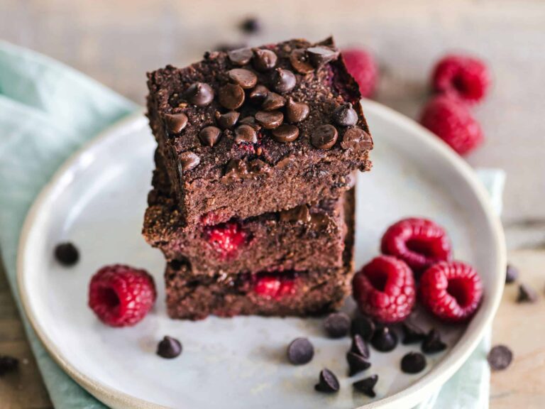 Close-up of deliciously indulgent chocolate raspberry brownies stacked on a ceramic plate with fresh raspberries. vegan desserts, refined sugar