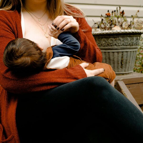 Intimate moment of a mother breastfeeding her child on a porch, symbolizing warmth and care. National Breastfeeding Week