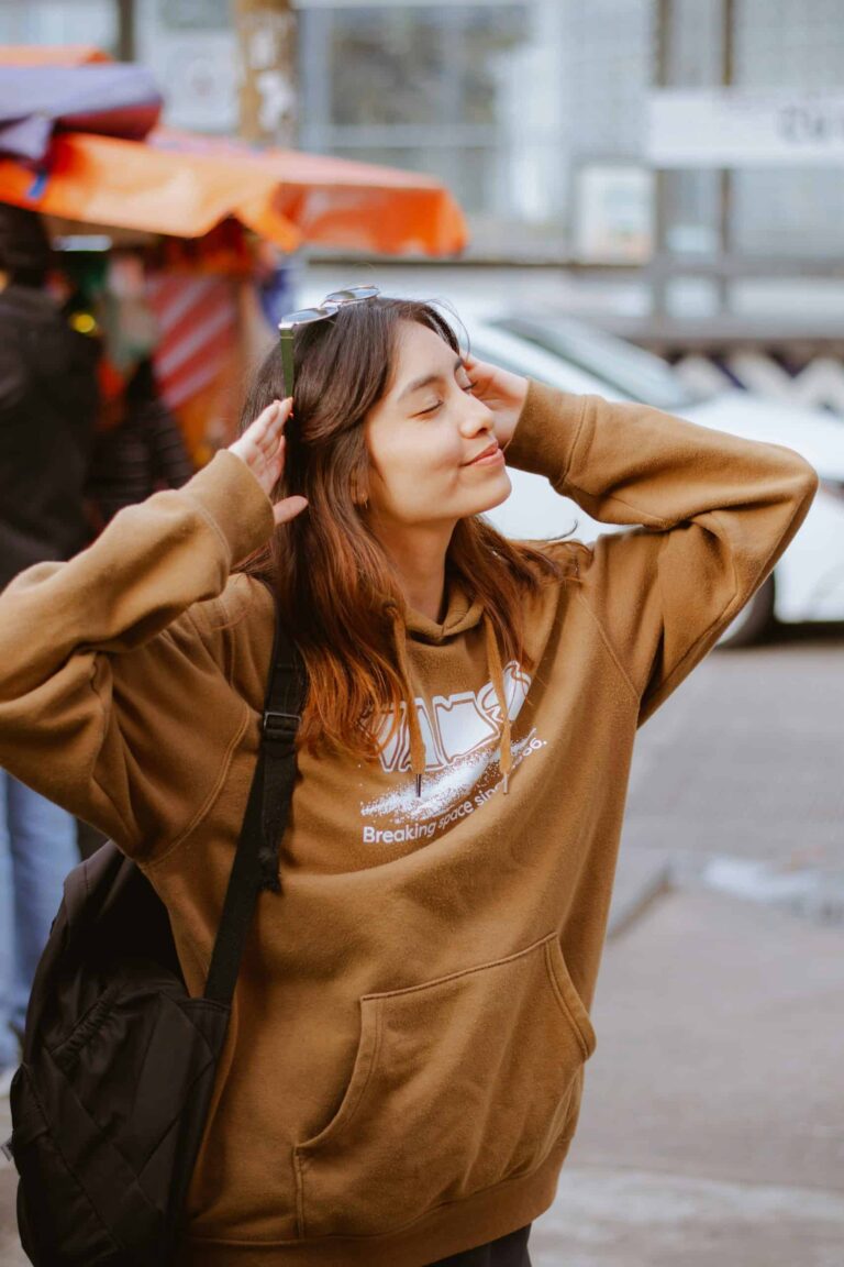 Woman in a brown hoodie enjoying a peaceful sunny day outdoors, reflecting on self-care and assessment. Photo by César O'neill via Pexels.