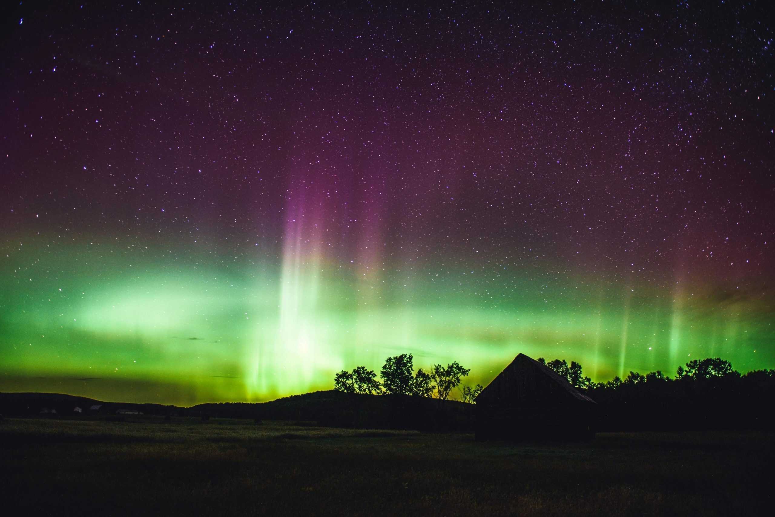 Stunning aurora borealis illuminating the night sky over a house and trees.