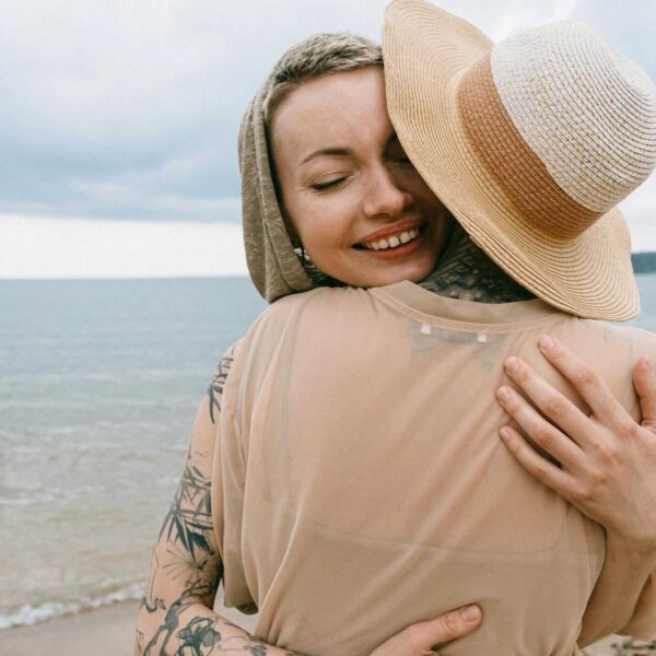 Two women embracing on a serene beach, expressing joy and friendship. Daily devotional