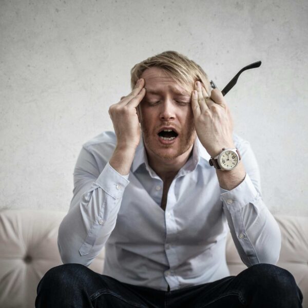 Stressed man sitting on couch, feeling overwhelmed and frustrated, expressing mental strain.