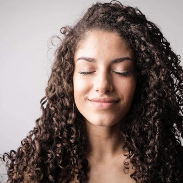 A close-up portrait of a smiling woman with curly hair, eyes closed, exuding happiness. Curly Hair Products