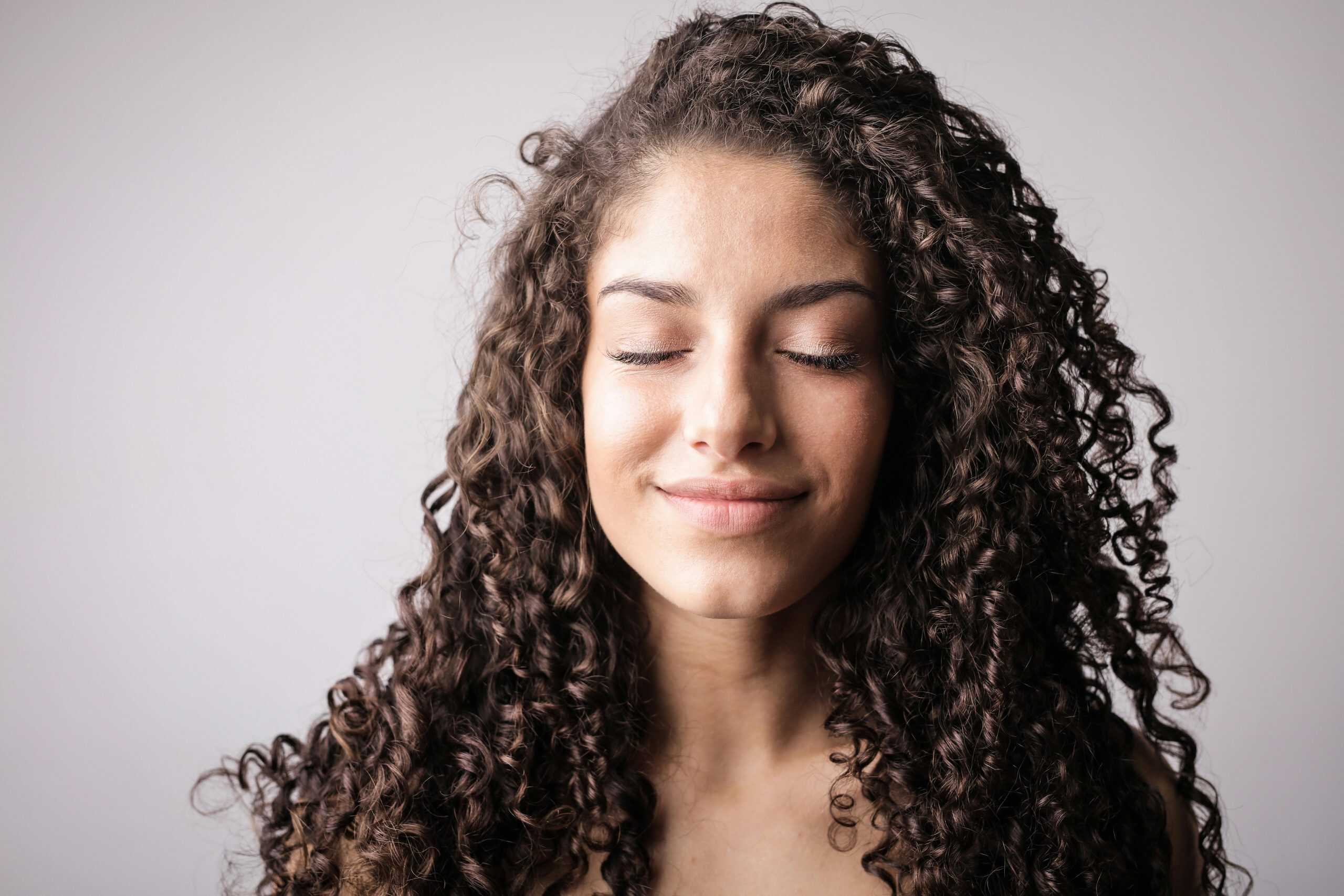 A close-up portrait of a smiling woman with curly hair, eyes closed, exuding happiness. Curly Hair Products