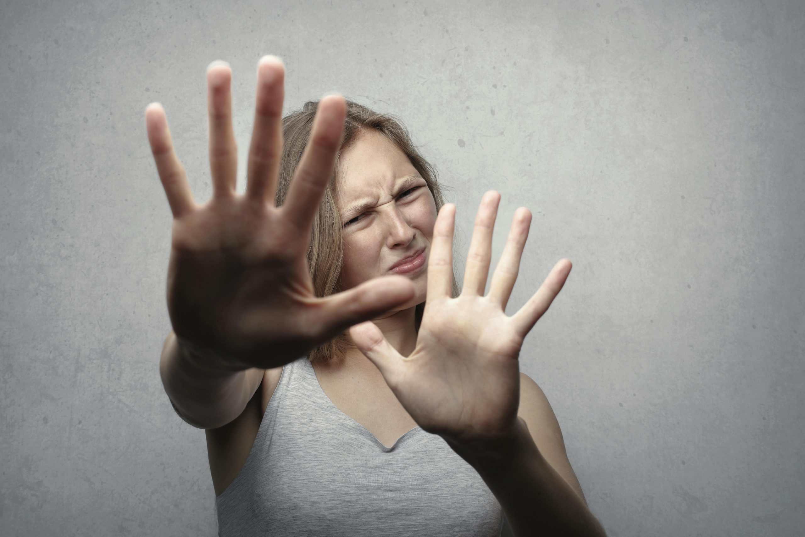 Portrait of a fearful woman in a gray tank top with hands pushed forward against a gray background. breakup, fearing
