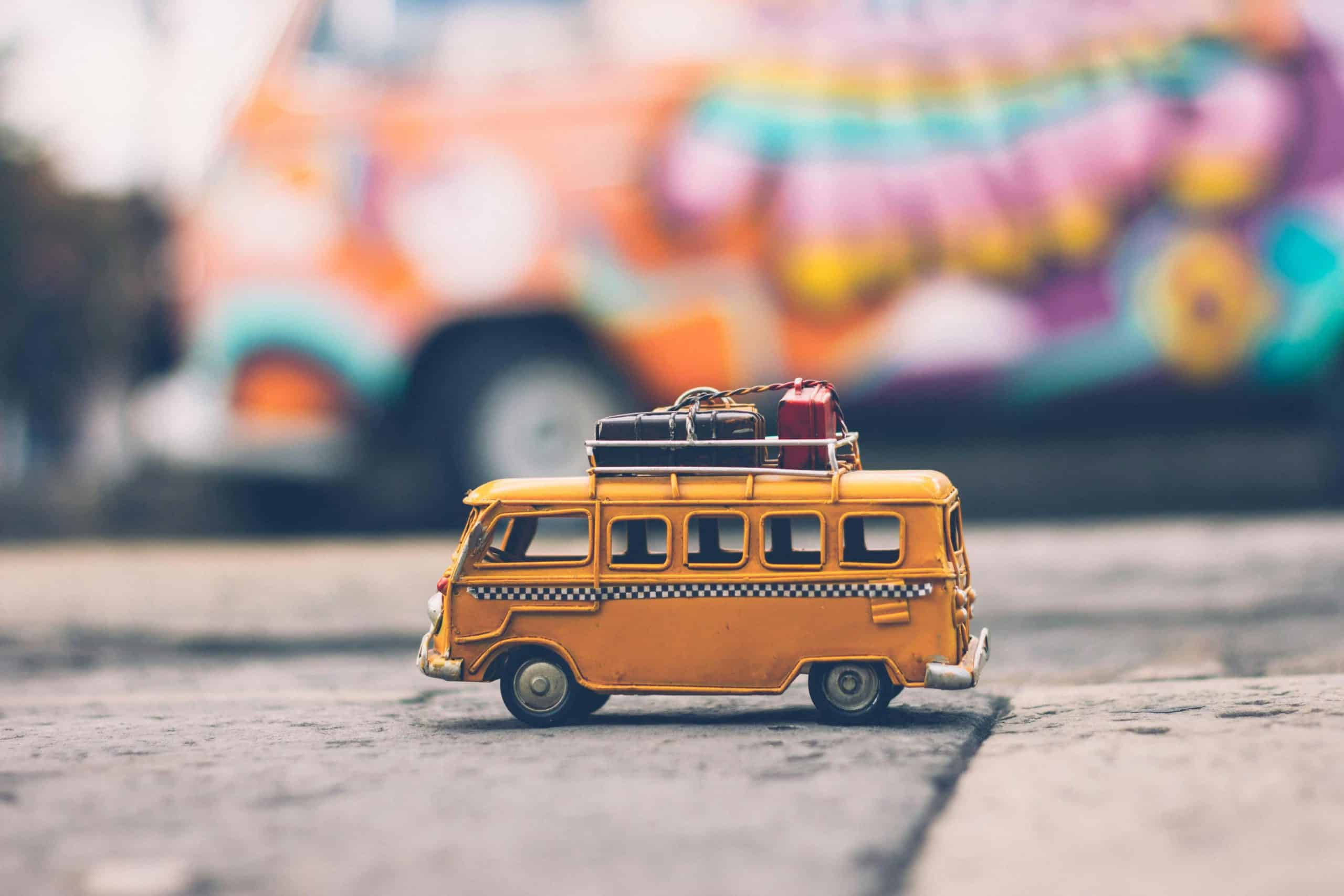 avoid jet lag, Close-up of a toy Volkswagen van with luggage, set against a colorful street backdrop, evoking summer travel vibes.