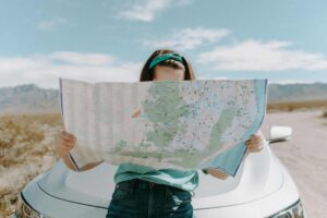 This is a photograph of a woman in front of a car in California. She is carefully reading a map. Immersive travel can provide ways for you to visit places in engaged ways. They can be opportunities for learning about new places.