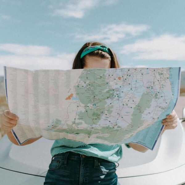 This is a photograph of a woman in front of a car in California. She is carefully reading a map. Immersive travel can provide ways for you to visit places in engaged ways. They can be opportunities for learning about new places.