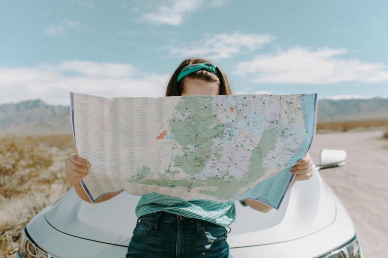 This is a photograph of a woman in front of a car in California. She is carefully reading a map. Immersive travel can provide ways for you to visit places in engaged ways. They can be opportunities for learning about new places.