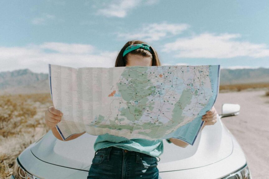 This is a photograph of a woman in front of a car in California. She is carefully reading a map. Immersive travel can provide ways for you to visit places in engaged ways. They can be opportunities for learning about new places.