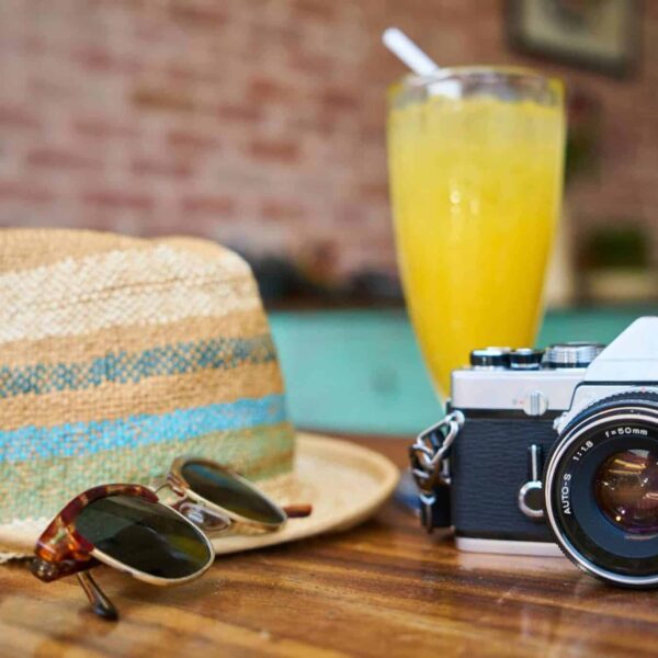 A stylish scene showcasing a vintage camera, hat, and orange juice, evoking summer travel vibes. Multi-generational travel trip