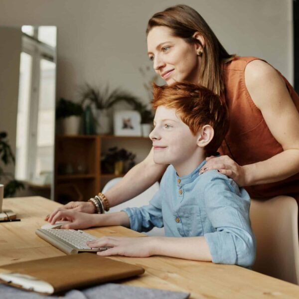 A mother and her child smiling while using a computer at home, focused on learning. Homeschooling