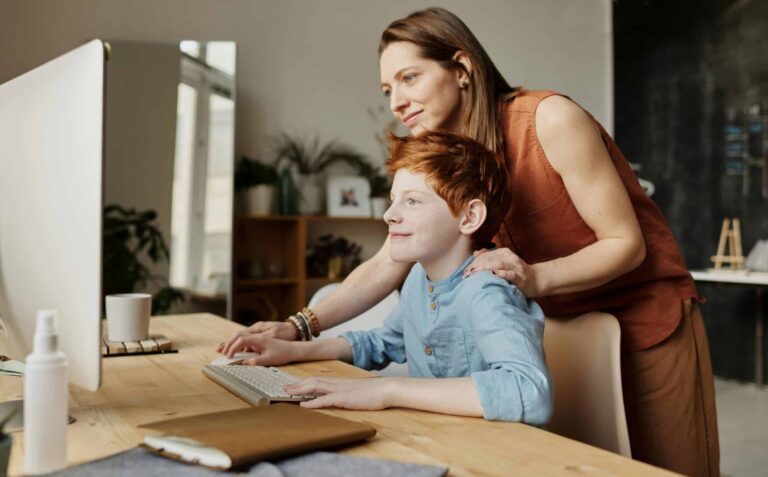 A mother and her child smiling while using a computer at home, focused on learning. Homeschooling