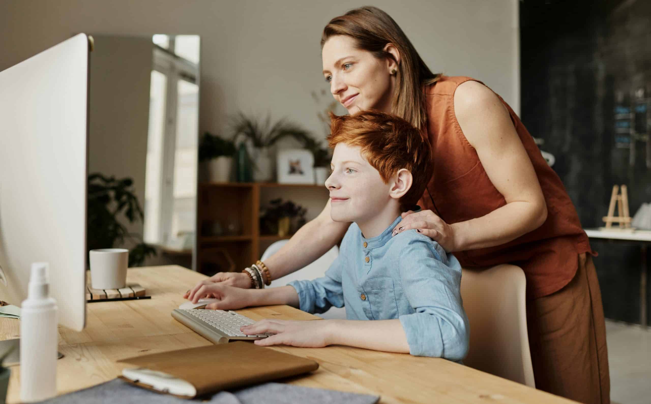 A mother and her child smiling while using a computer at home, focused on learning. Homeschooling