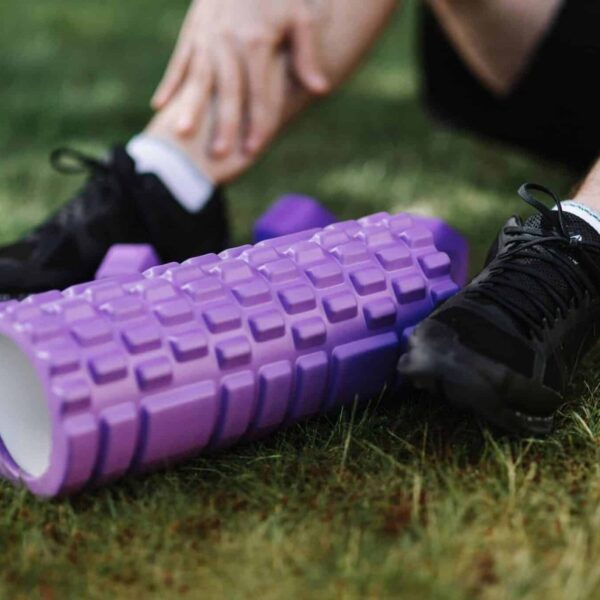 Black sneakers and purple foam roller on grass, outdoor fitness scene. Sore Muscle Recovery
