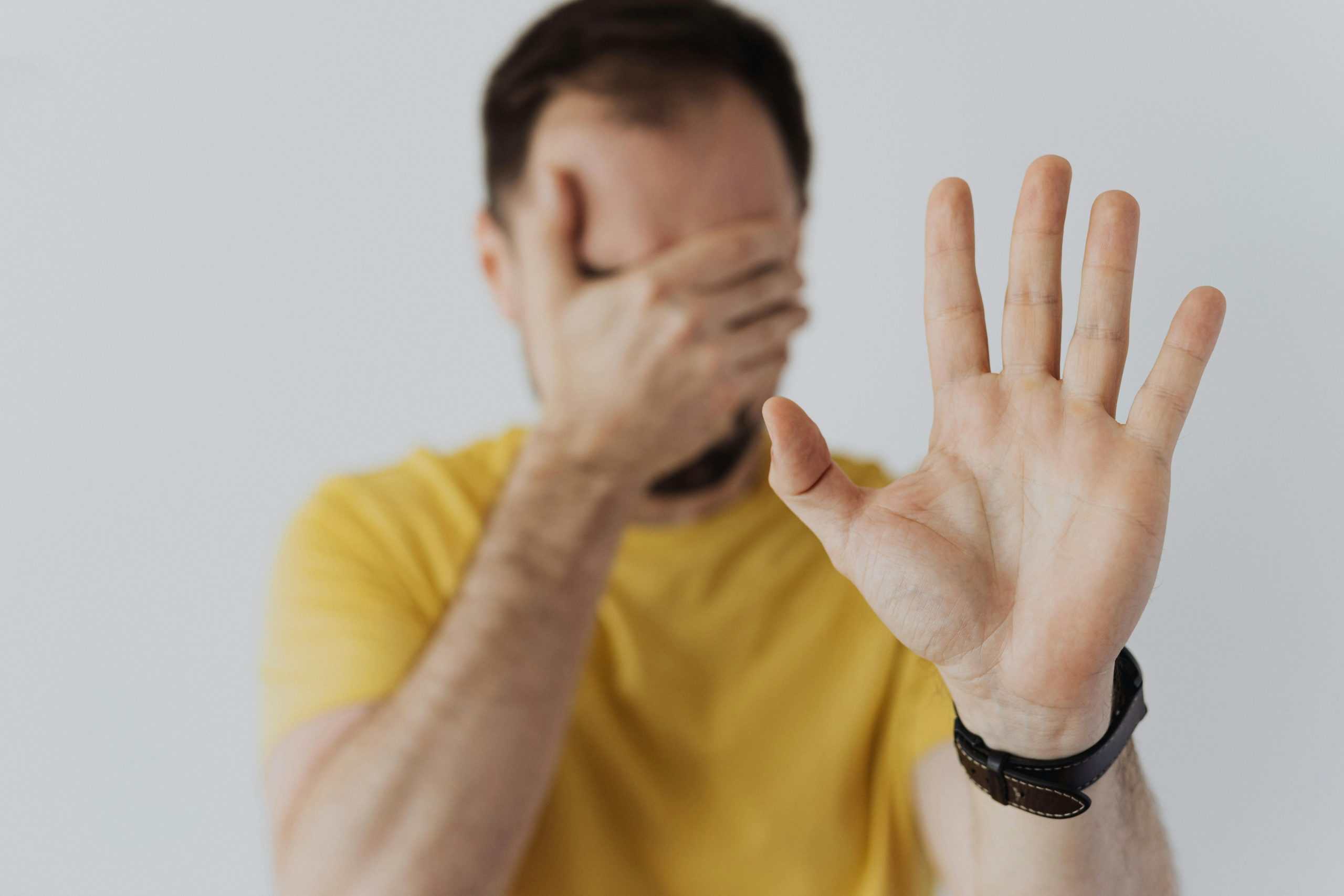 Close-up of a man covering his face and showing a stop gesture with his hand. emotionally unavailable