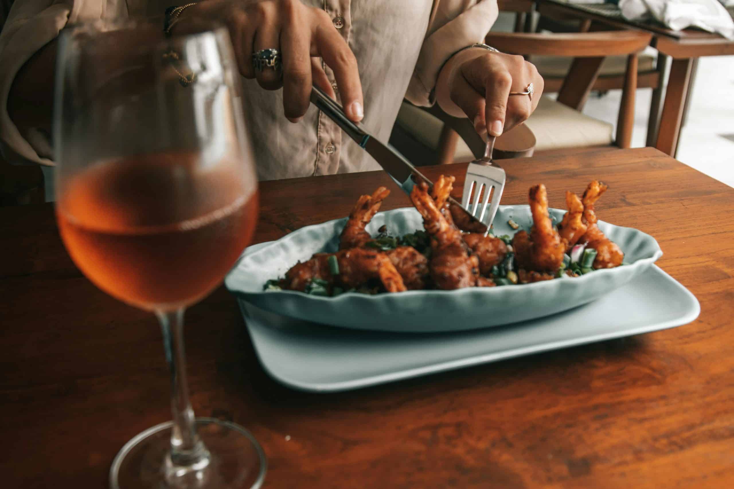 A person enjoys gourmet fried shrimp with a glass of rosé wine at an elegant dining setting. Wine pairing 