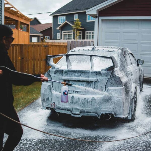Side view of faceless male in black clothing washing car with foam in yard of house in daytime. Pressure Washer Recall