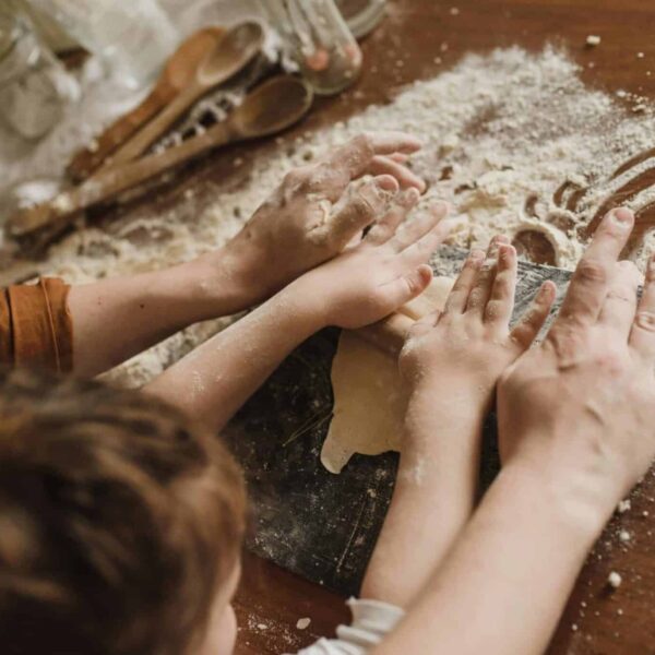 A parent and child bonding while kneading dough in a messy kitchen environment. bake with kids