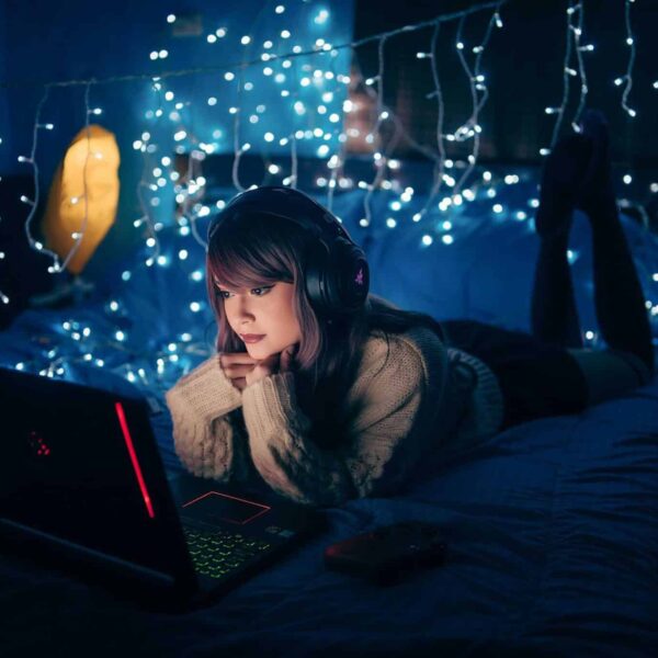 bed styling, A young woman in a cozy room, wearing headphones and using a laptop, surrounded by warm fairy lights.