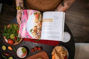Close-up of chef holding cookbook over Mexican ingredients on table. Best cookbooks