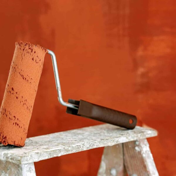 Glidden, Detailed image of a paint roller resting on a ladder with a vibrant orange wall in the background.