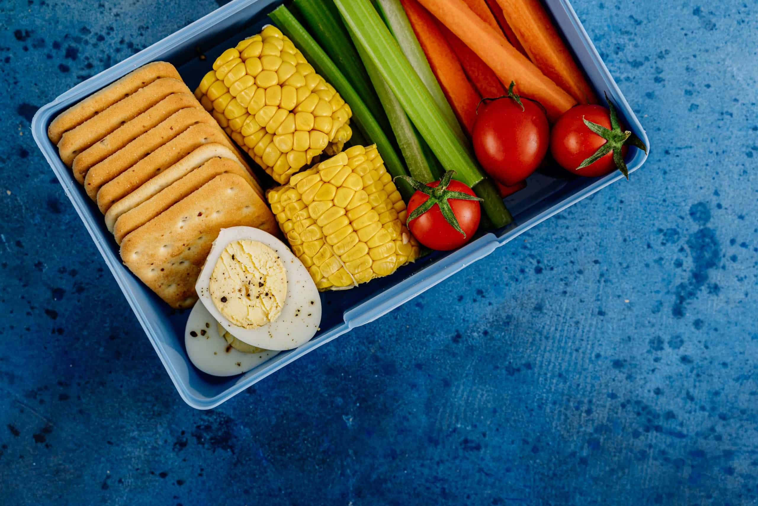 A vibrant lunchbox filled with nutritious vegetables, eggs, and crackers for a healthy meal. Lunchbox wellness