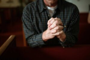 A man in a checked shirt praying in a church, hands clasped together. daily devotion