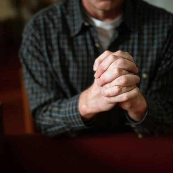 A man in a checked shirt praying in a church, hands clasped together. daily devotion