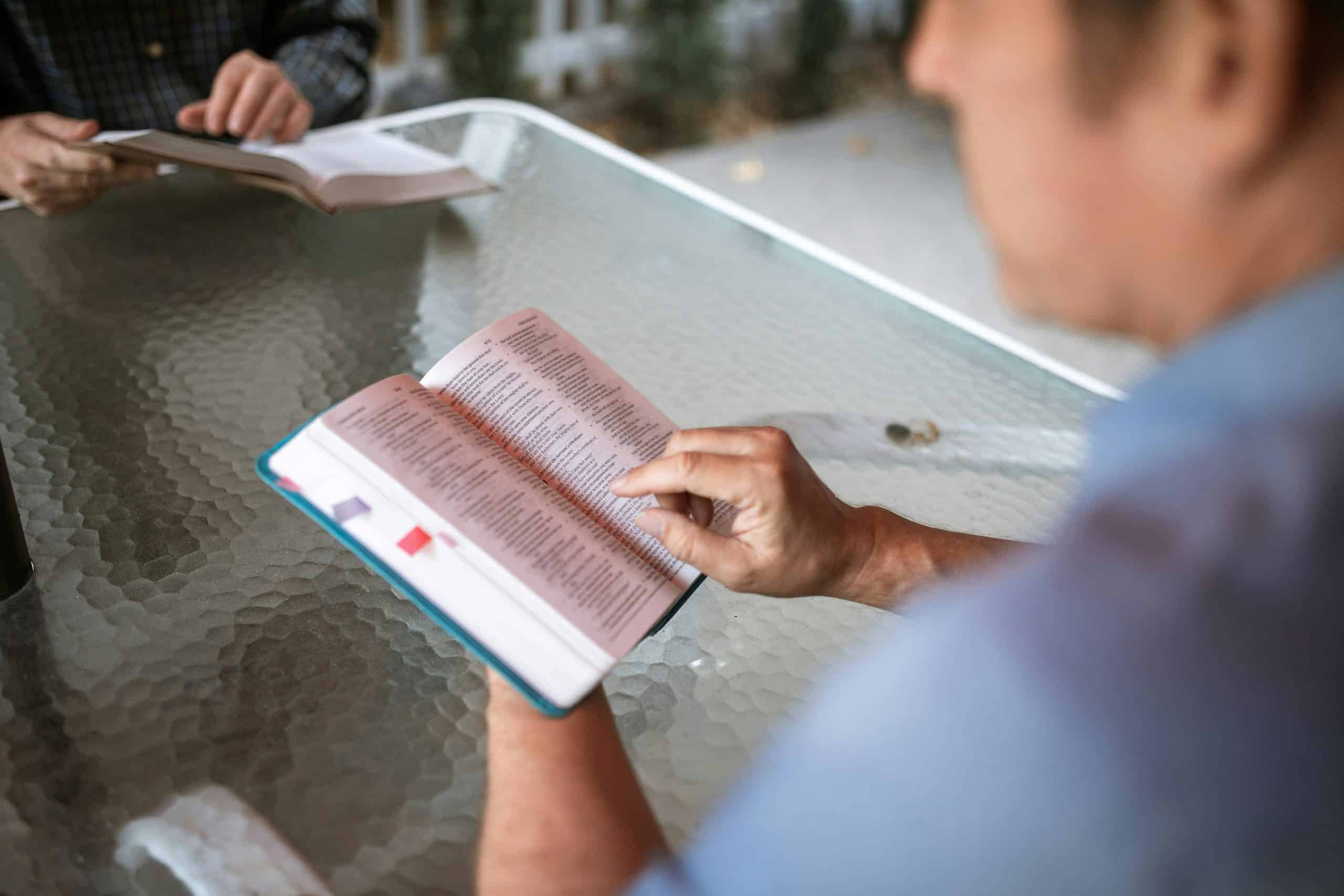 Two adults engaged in Bible study at a glass table outdoors, promoting faith and connection. scripture, emotional maturity